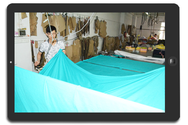 (年轻的裁床师傅边铺布,边检查面料是否有瑕疵)